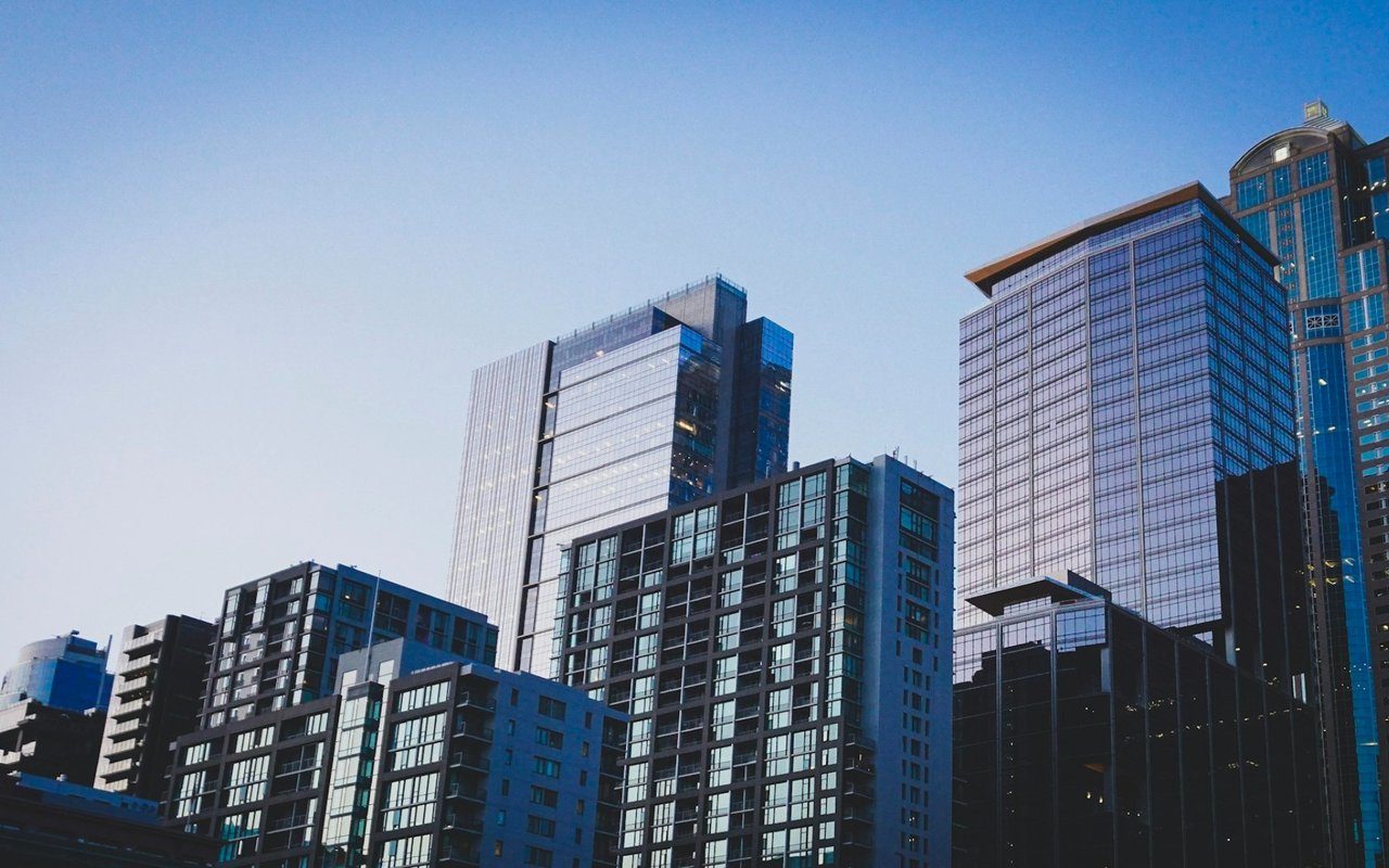 Modern glass high-rises against a clear blue sky, viewed from below.