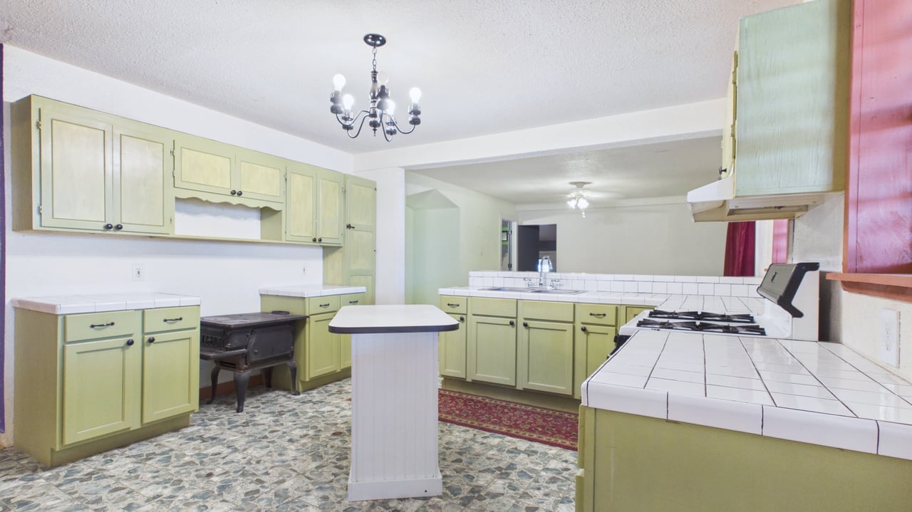 Kitchen with pale green cabinets, tiled counters, a central island, and a freestanding wood stove.
