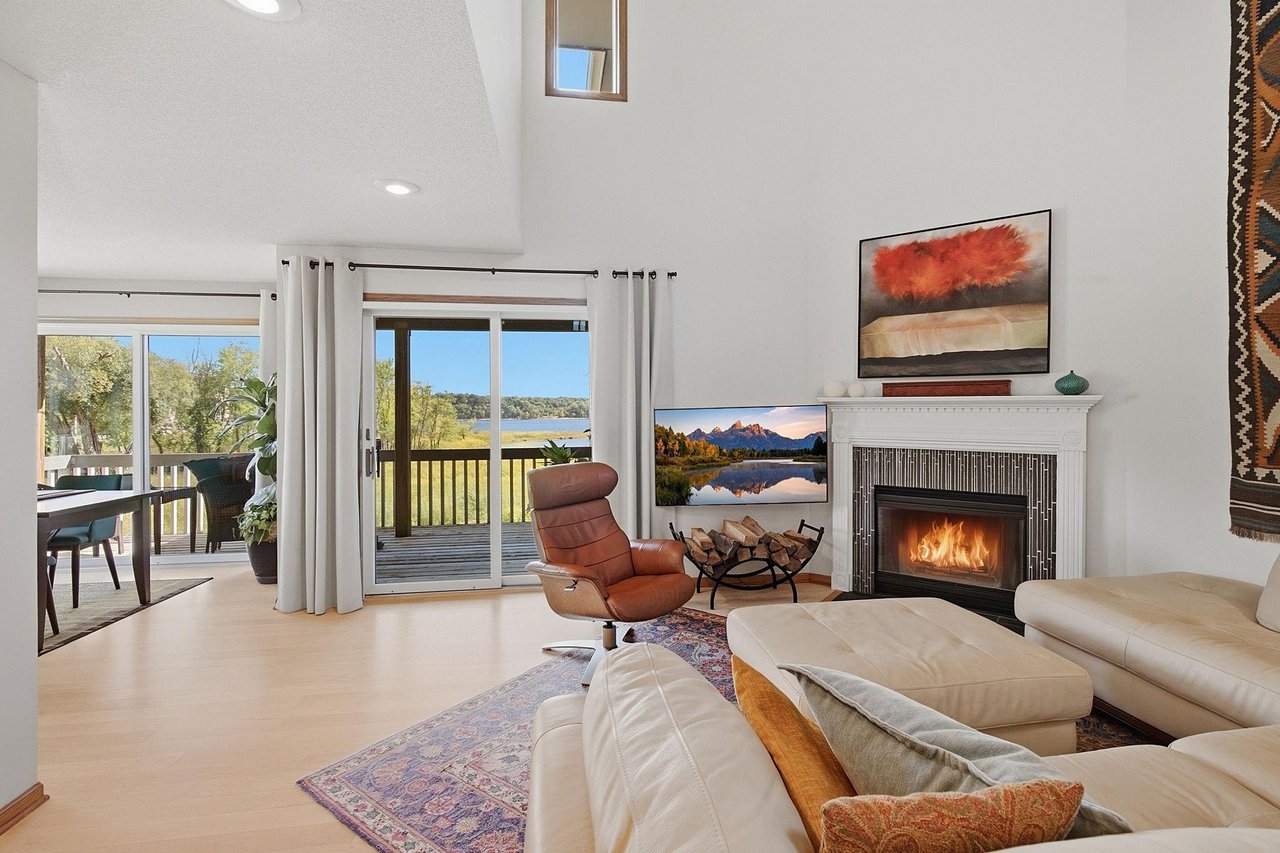 Living room with a vaulted ceiling, white fireplace, and water views through large windows.
