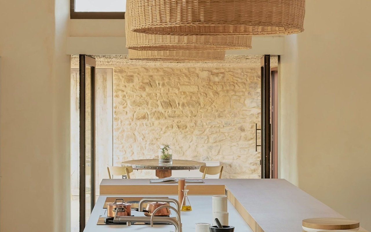 Kitchen with a long island and copper cookware opening onto a dining area with a rustic stone wall.