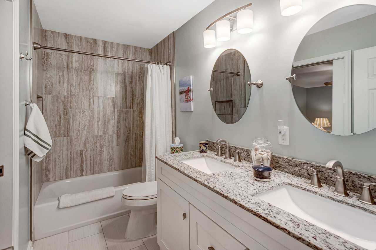 Bathroom with double-sink vanity, granite countertop, and tiled tub and shower.