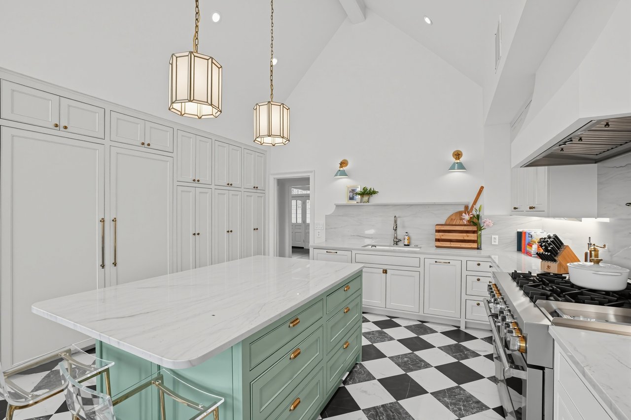 Bright kitchen with a vaulted ceiling, mint island, marble counters, checkerboard floors, and stainless-steel range.