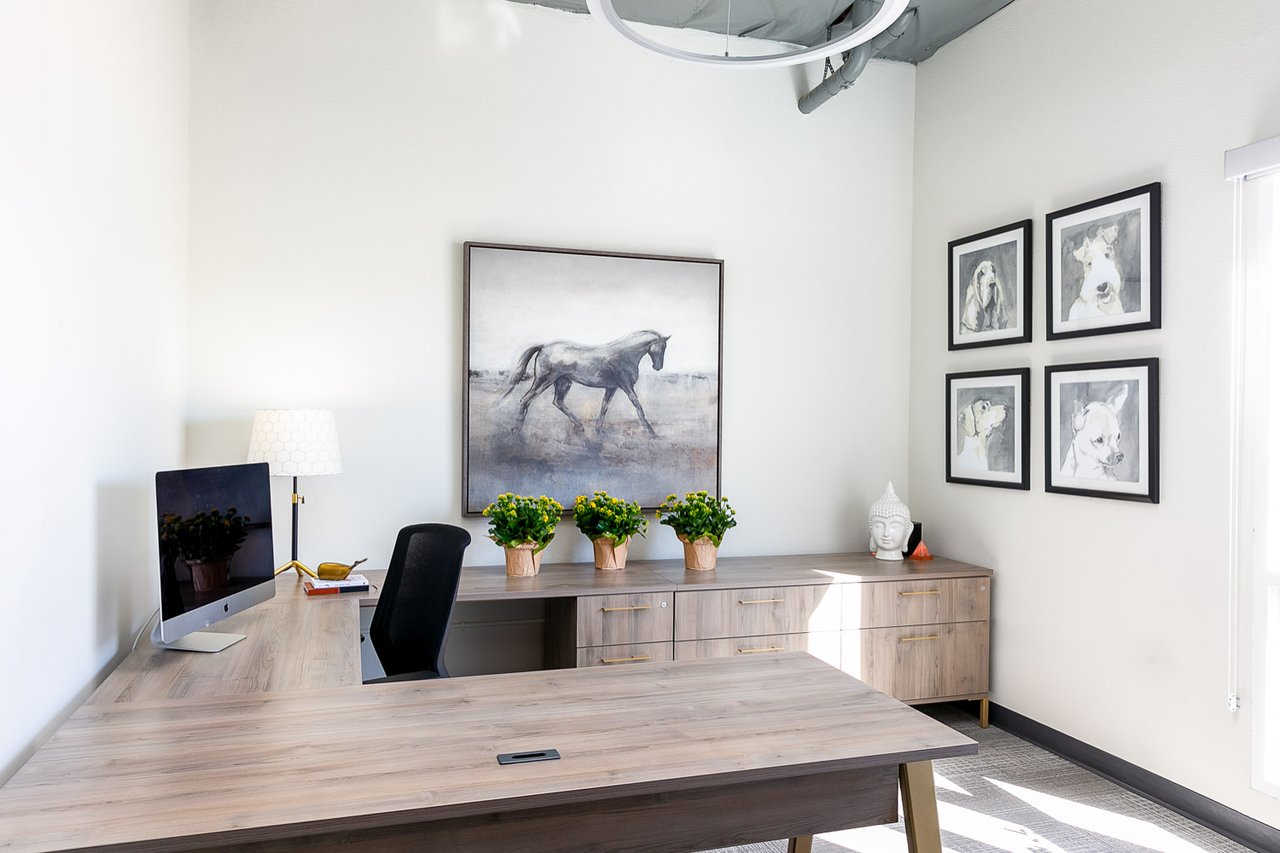 Bright office with a large wood desk, computer workstation, and framed horse and dog artwork.