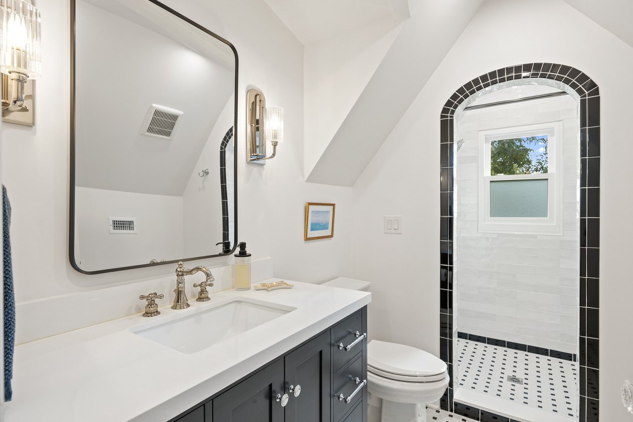 Bathroom with a dark vanity and an arched, black-trimmed shower beside a window.