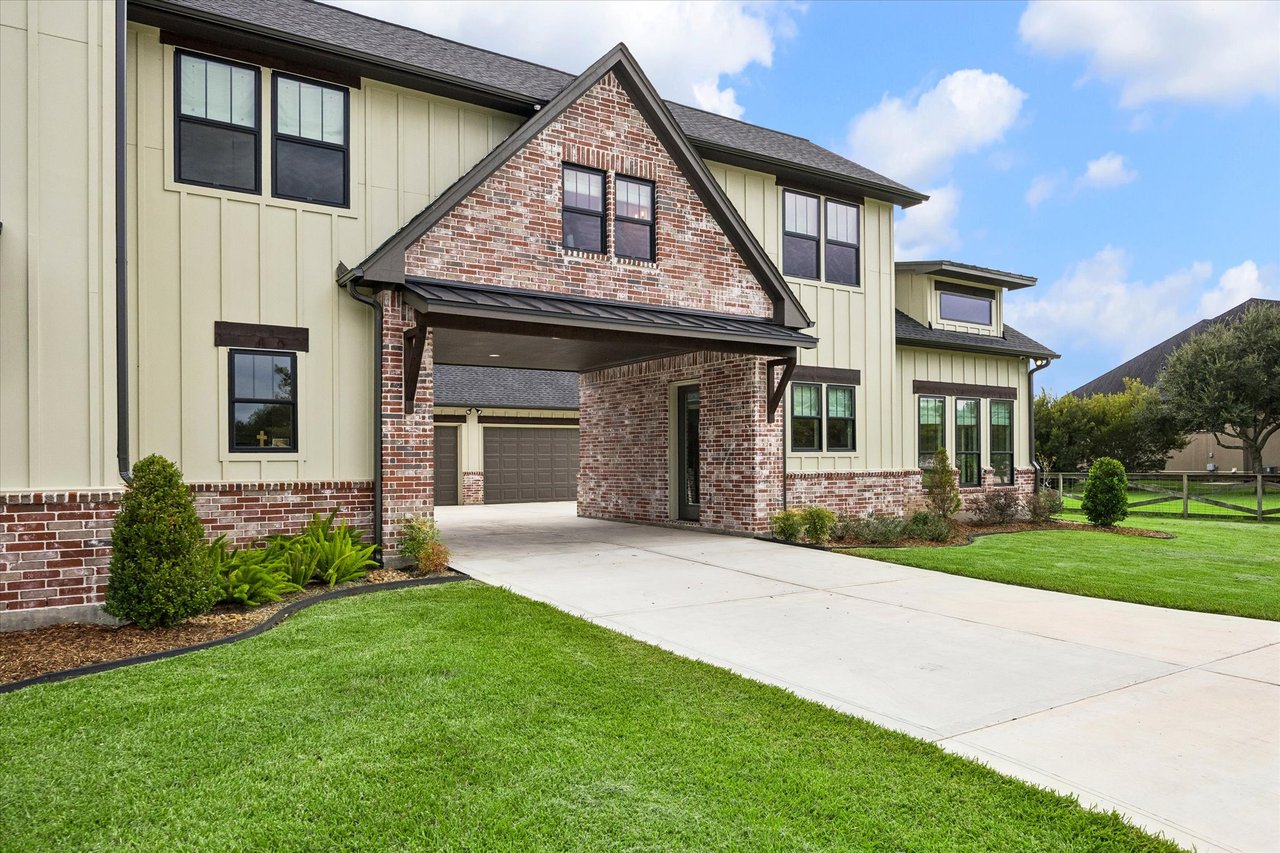 Two-story home with a brick entry, covered driveway, landscaped beds, and broad green lawn.
