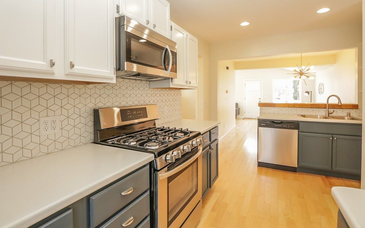 Kitchen with stainless steel gas range, geometric tile backsplash, gray cabinets, and light wood floors.