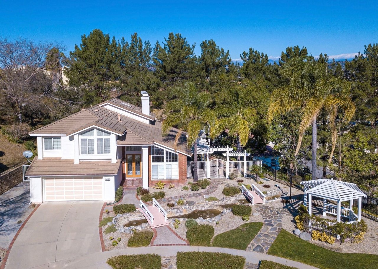 Two-story home with a tiled roof, landscaped yard, stone paths, pergola, and gazebo.