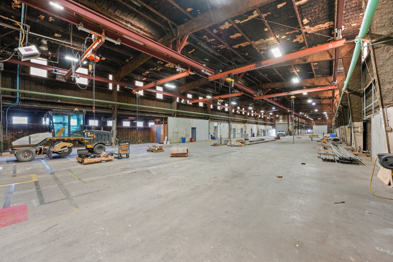 Warehouse interior with overhead bridge cranes, exposed ceiling beams, and a wide concrete floor.