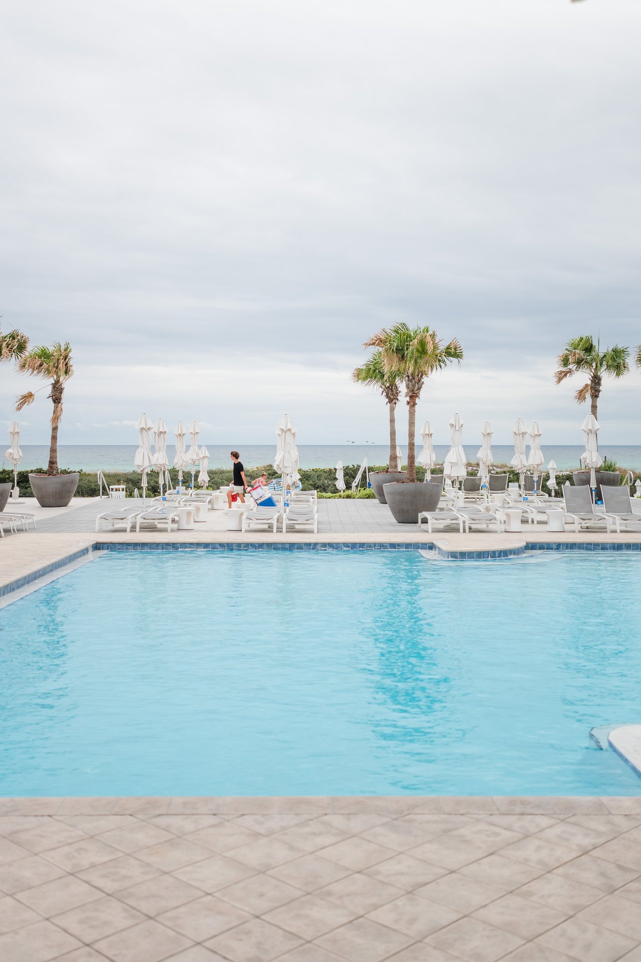 Crystal-blue beachfront pool lined with white loungers and palms opening onto the Gulf at WaterColor on 30A, Florida