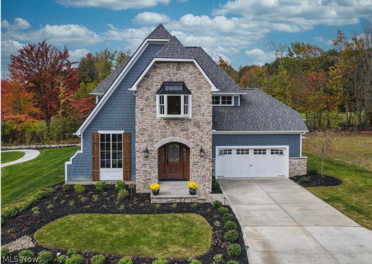 Blue-sided home with a stone facade, steep roof, white garage door, and landscaped front yard.