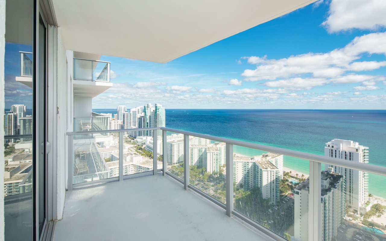 High-rise balcony with glass railings overlooking the ocean and coastal skyline.