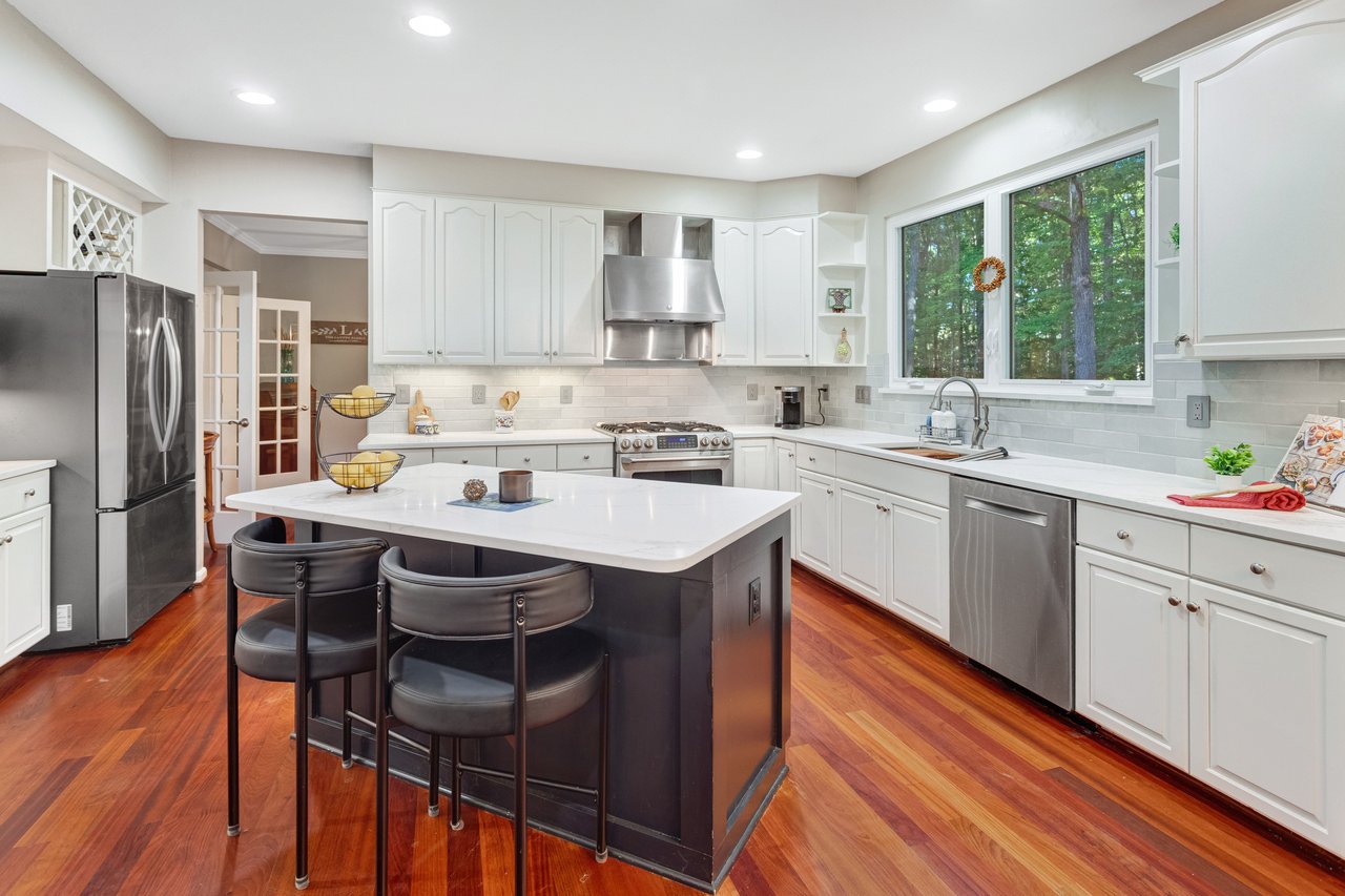 Kitchen with a large dark island, white cabinetry, stainless appliances, and hardwood floors.