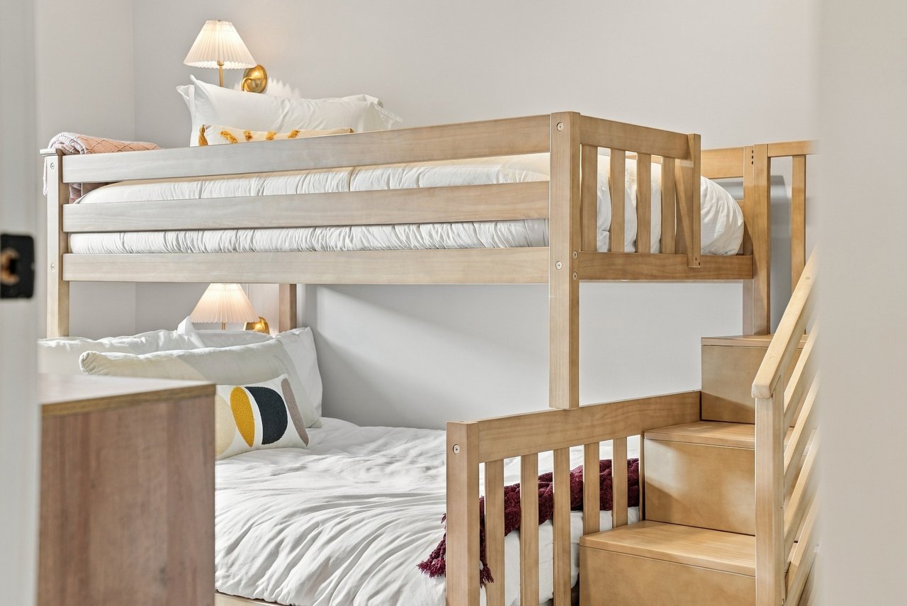 Bedroom with a light wood bunk bed, built-in stairs, and white bedding.