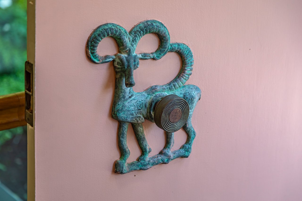Turquoise sculptural door knocker mounted on a pale pink door.