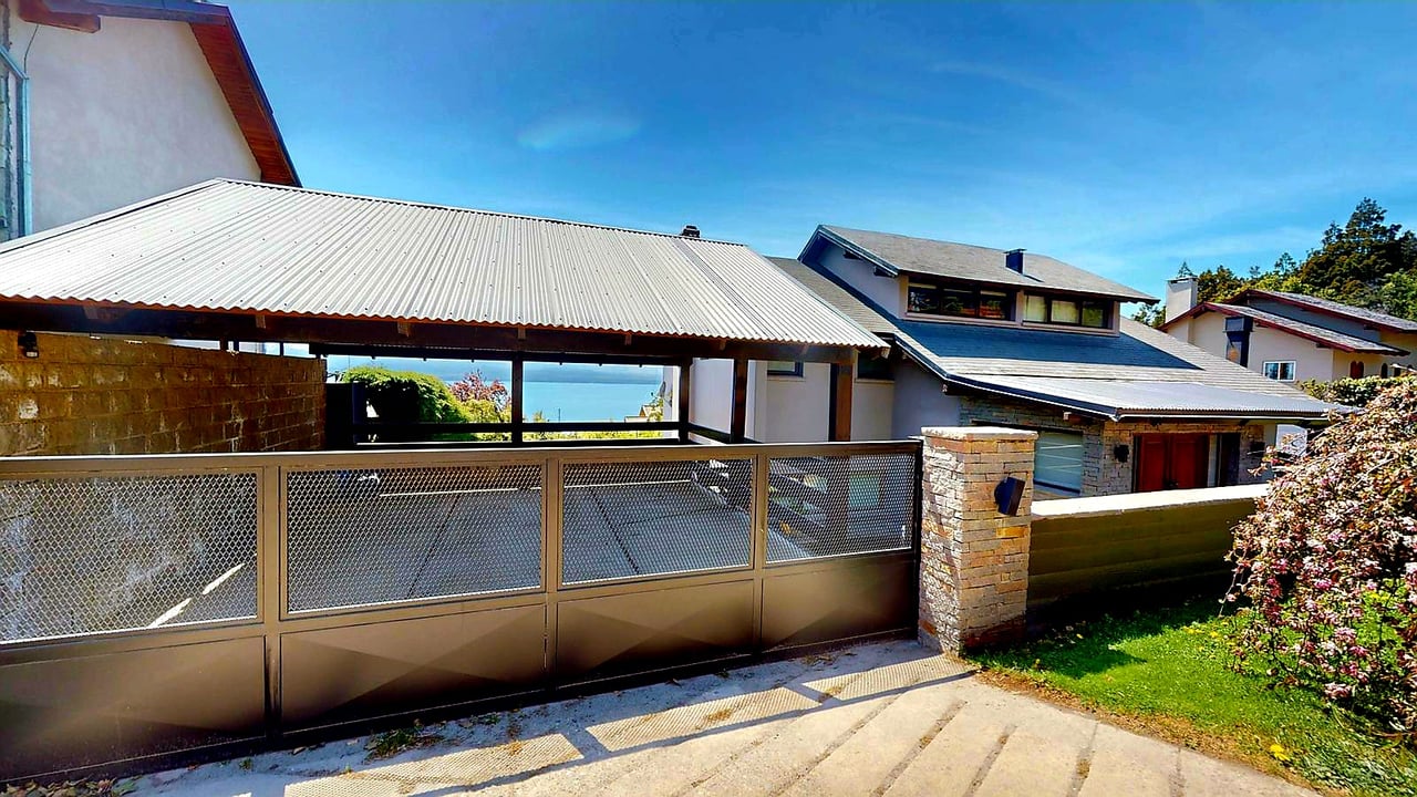 Modern house behind a wide metal gate, with water visible through the covered entrance.