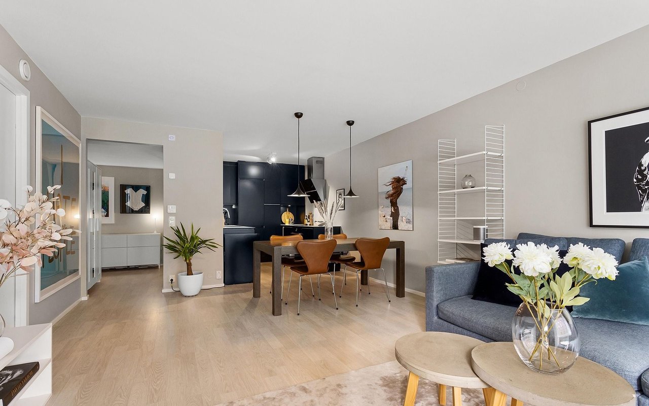 Open-plan living room with a blue sofa, round coffee tables, and a dining area beside a dark kitchen.