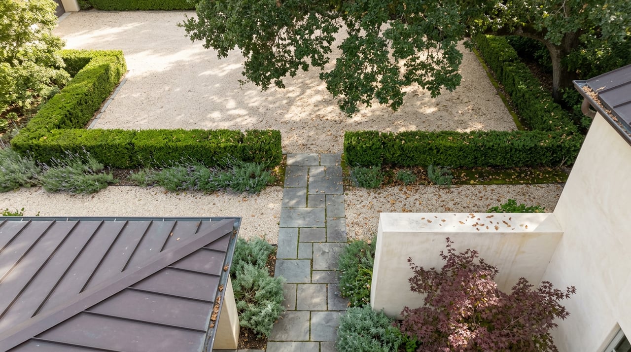 Courtyard from above, with gravel, clipped hedges, bluestone path, and metal roof beside stucco.