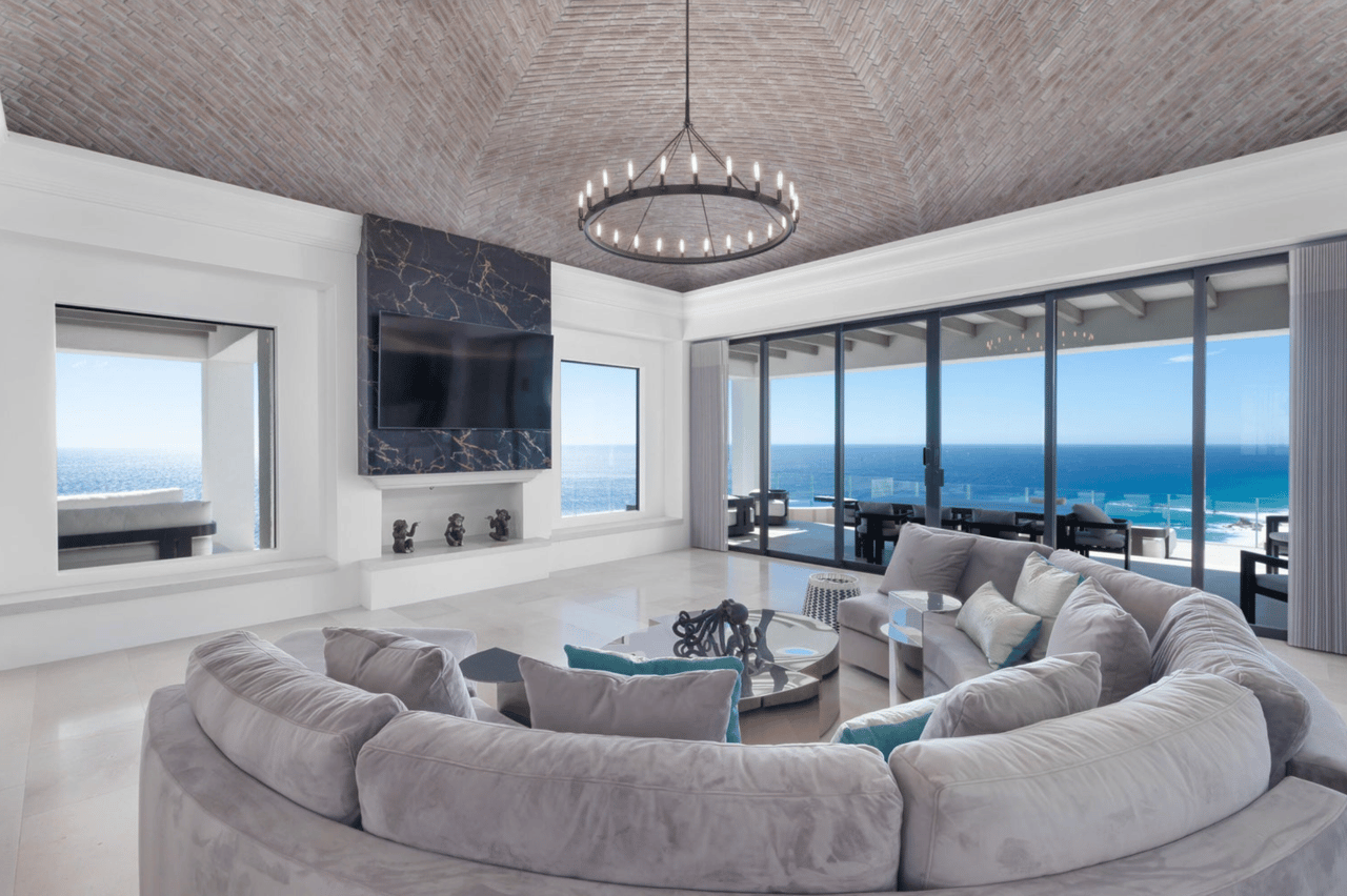 Ocean-view living room with a curved sectional, marble TV wall, and vaulted brick ceiling.
