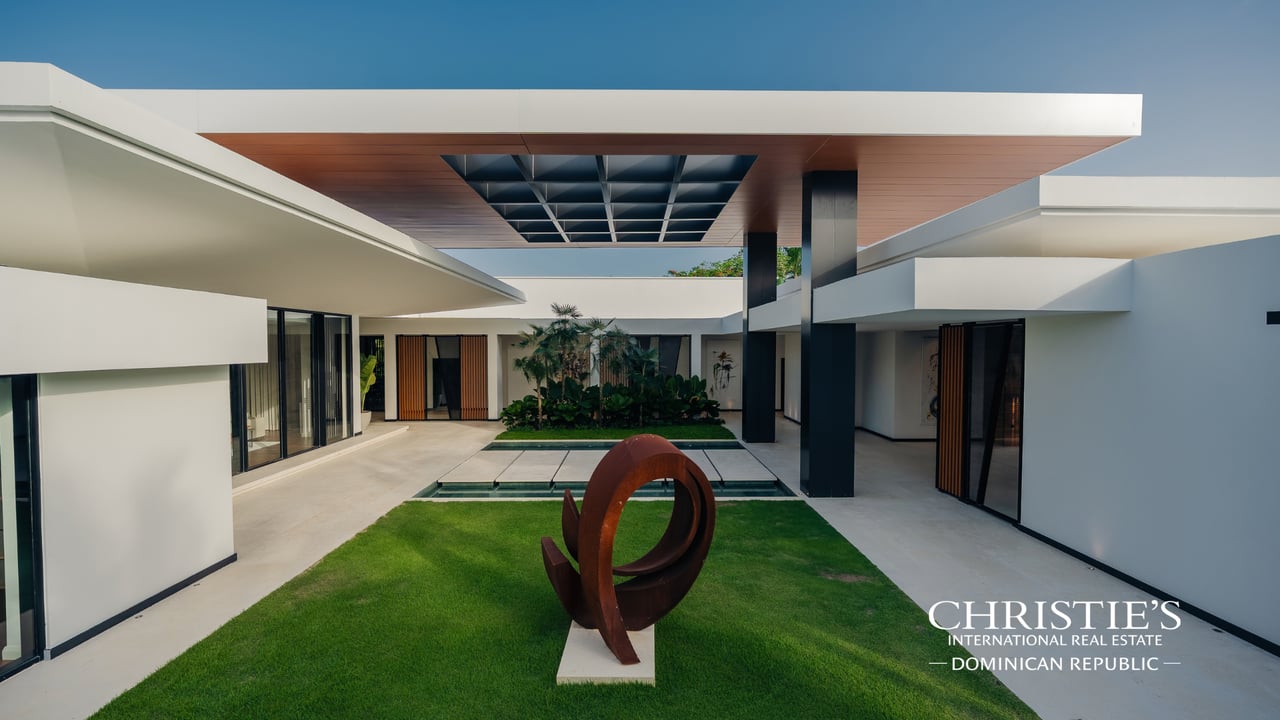 Modern white villa courtyard with a reflecting pool, lawn sculpture, and wood-paneled canopy.