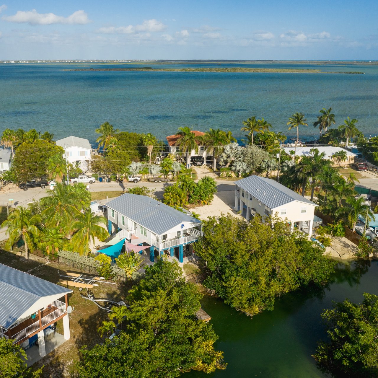 Aerial view of palm-lined waterfront homes beside a canal, with open blue water beyond.