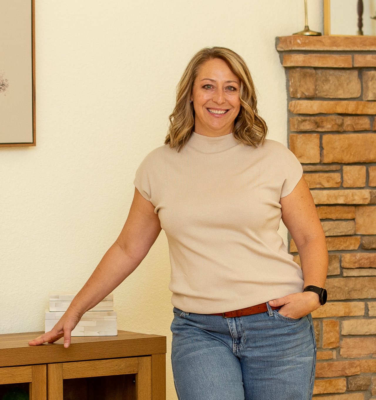 Tera Donahoo smiles beside a wooden console table and stone fireplace.