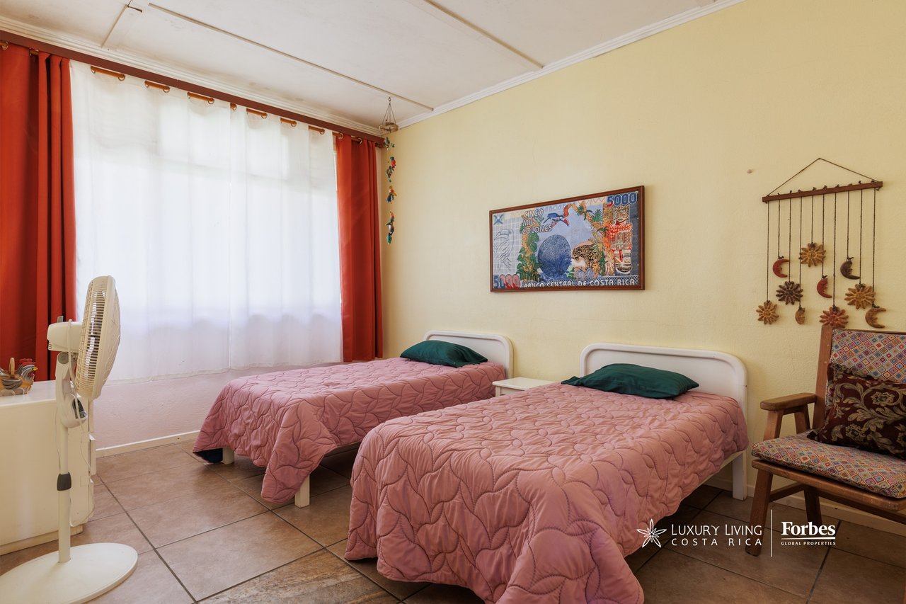 Bedroom with two twin beds covered in pink quilts beside a large curtained window.