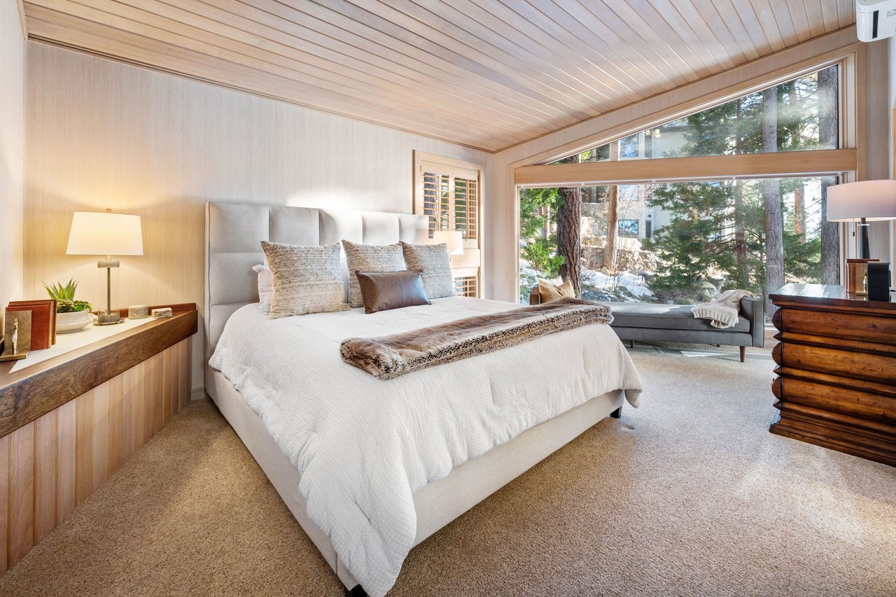 Bedroom with a king-size bed and large windows overlooking pine trees.