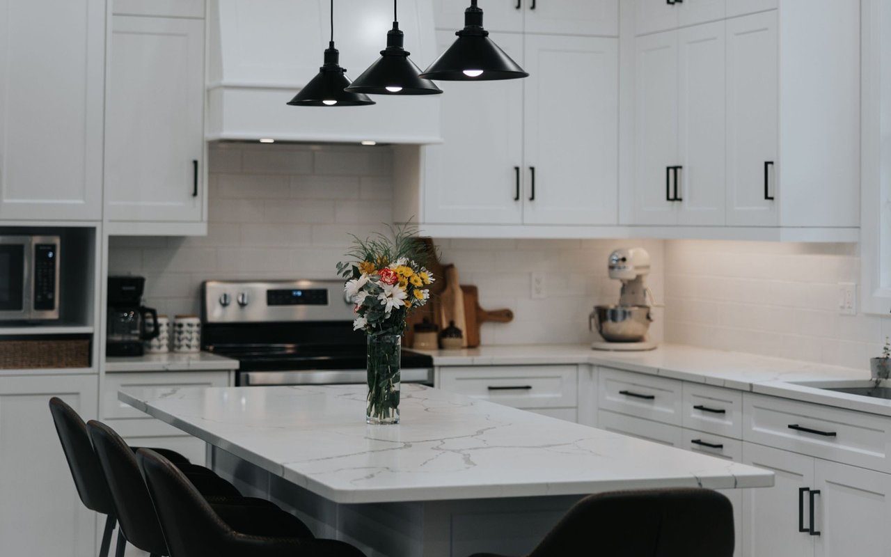 Modern white kitchen with a marble-patterned island, black pendant lights, and flowers in a vase.