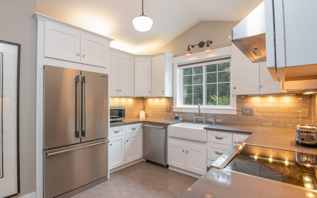 Bright kitchen with white cabinets, stainless steel appliances, and a farmhouse sink beneath a large window.