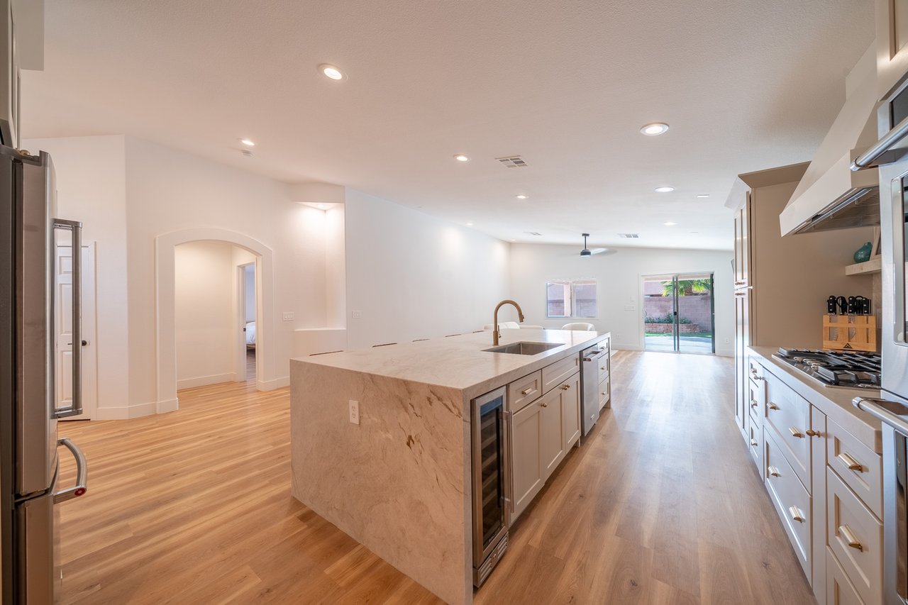 Open kitchen with a large marble waterfall island, white cabinets, stainless steel appliances, and wood floors.