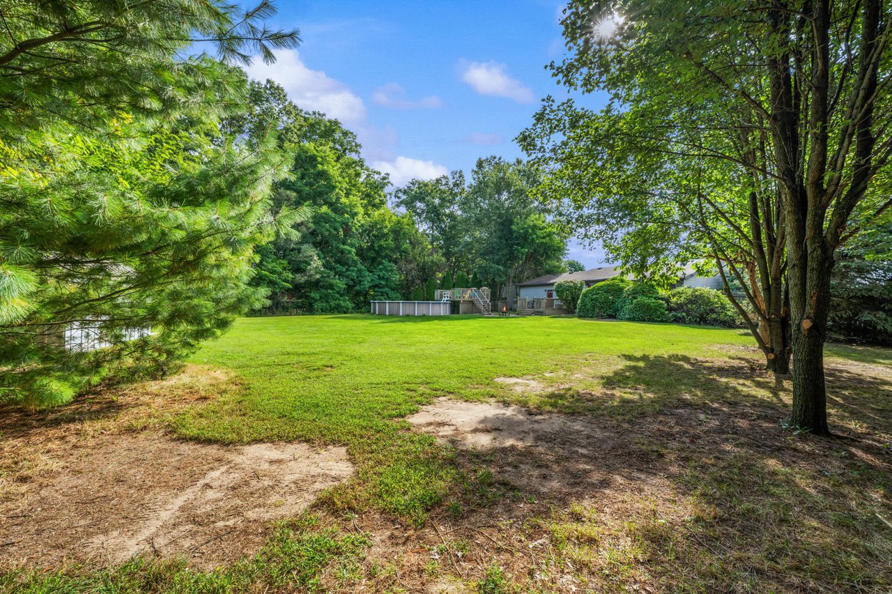Backyard with a broad lawn, mature trees, and a raised swimming pool beside the house.