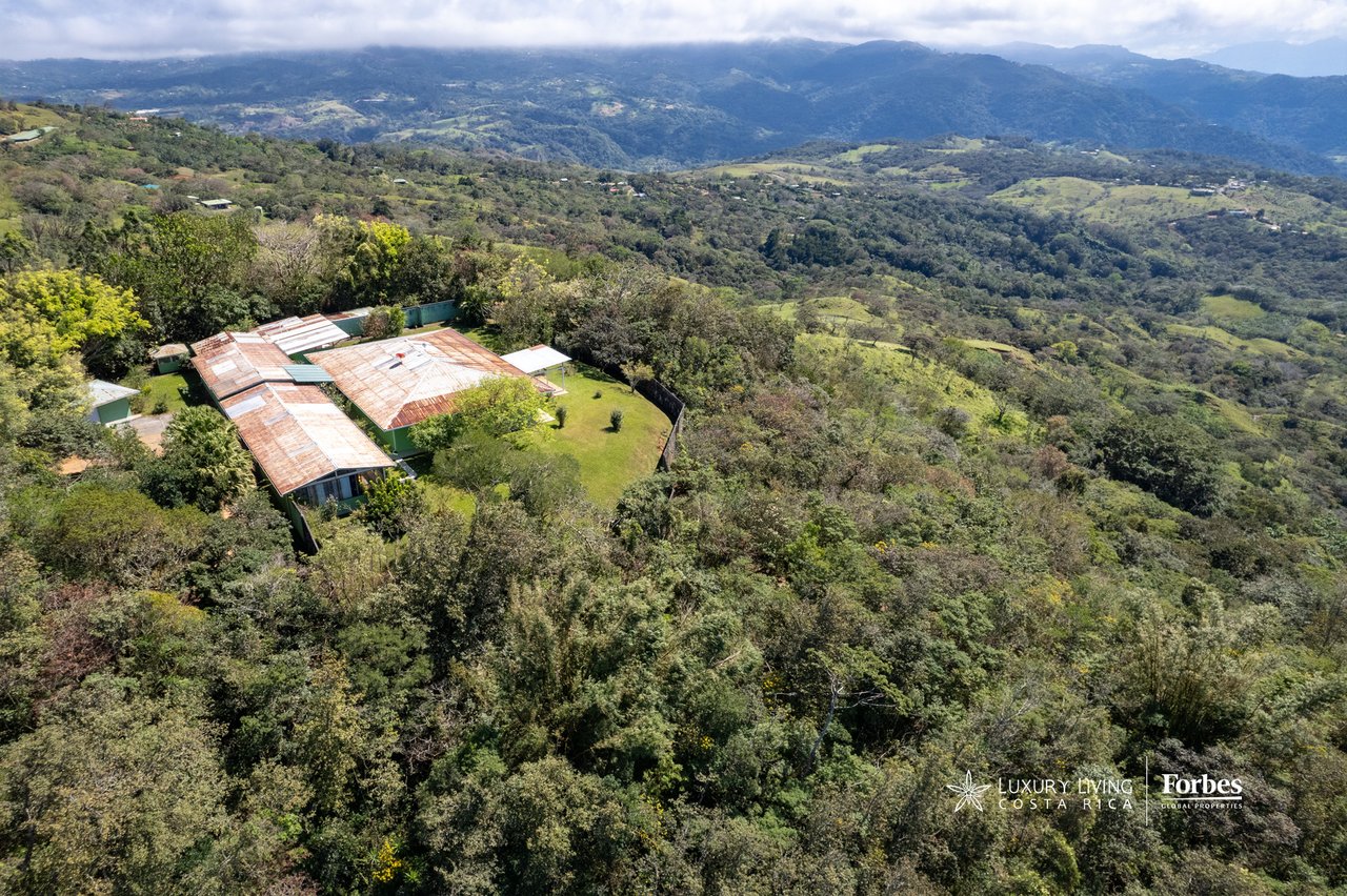 Mountain retreat among trees, overlooking a broad valley and distant forested ridges.