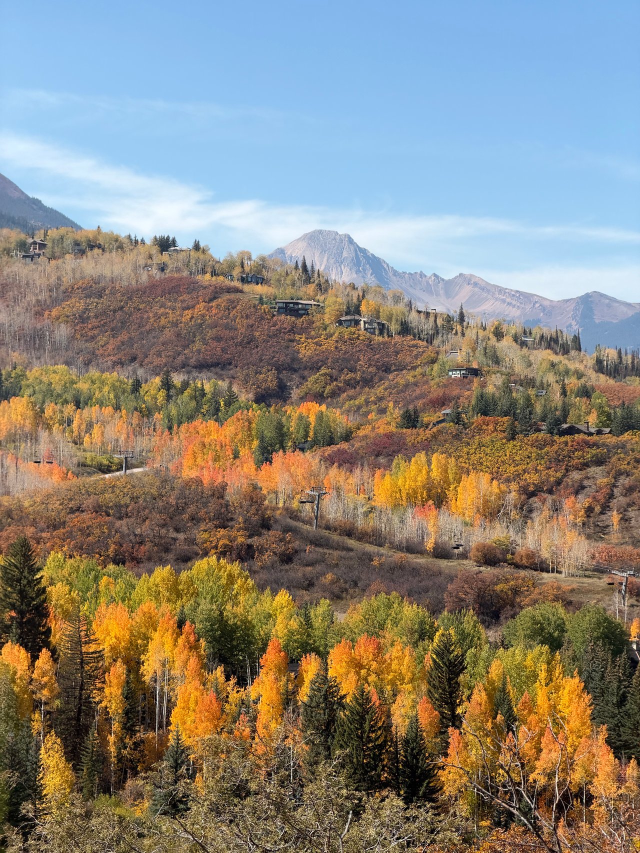 Autumn foliage blankets mountain hillsides dotted with homes beneath a clear blue sky.