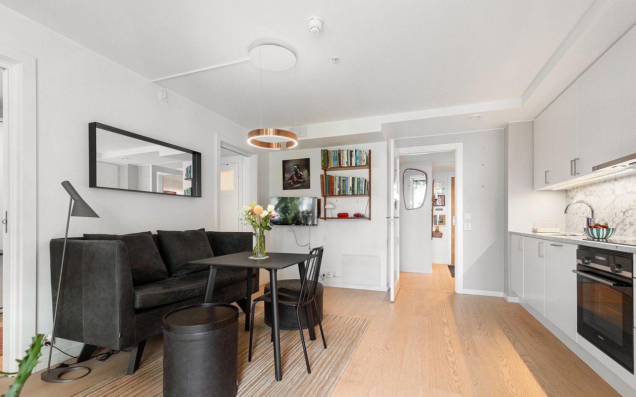 Open-plan living room and kitchen with a dark sofa, light wood floors, and white cabinetry.