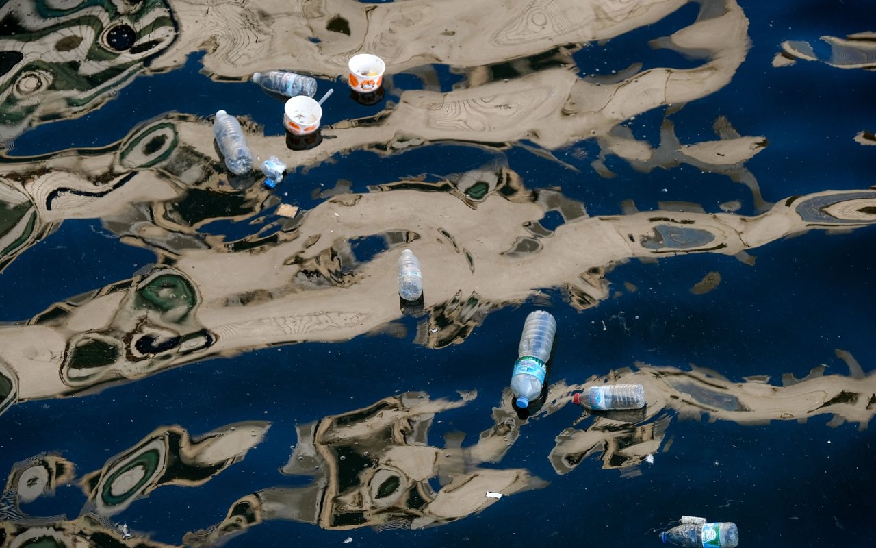 Plastic bottles and cups floating on dark, polluted water.