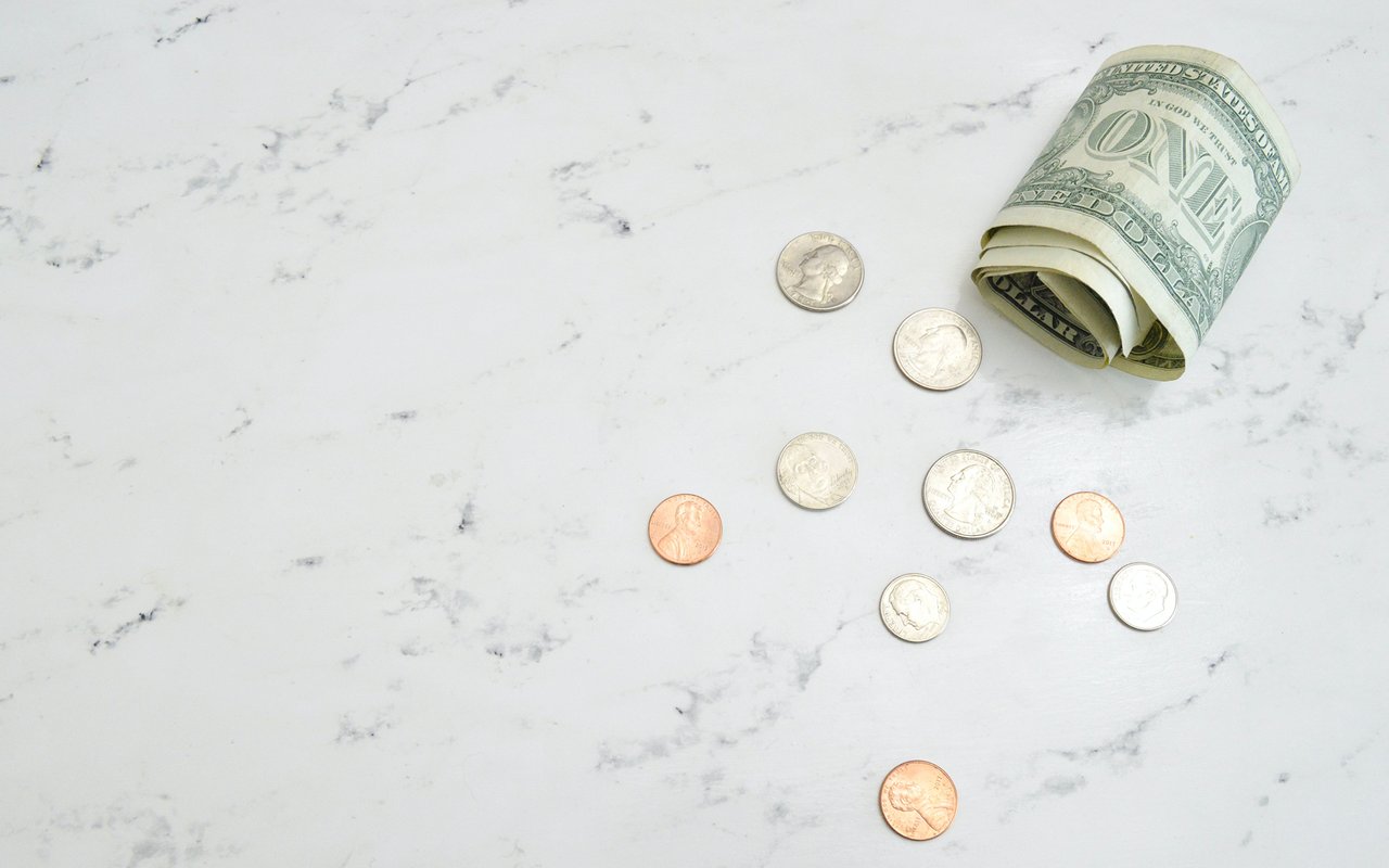 A rolled dollar bill and scattered coins on a white marble surface.