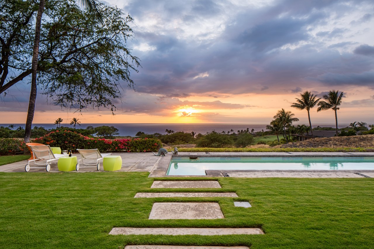 Oceanfront pool and lawn at sunset, with palm trees and lounge chairs.