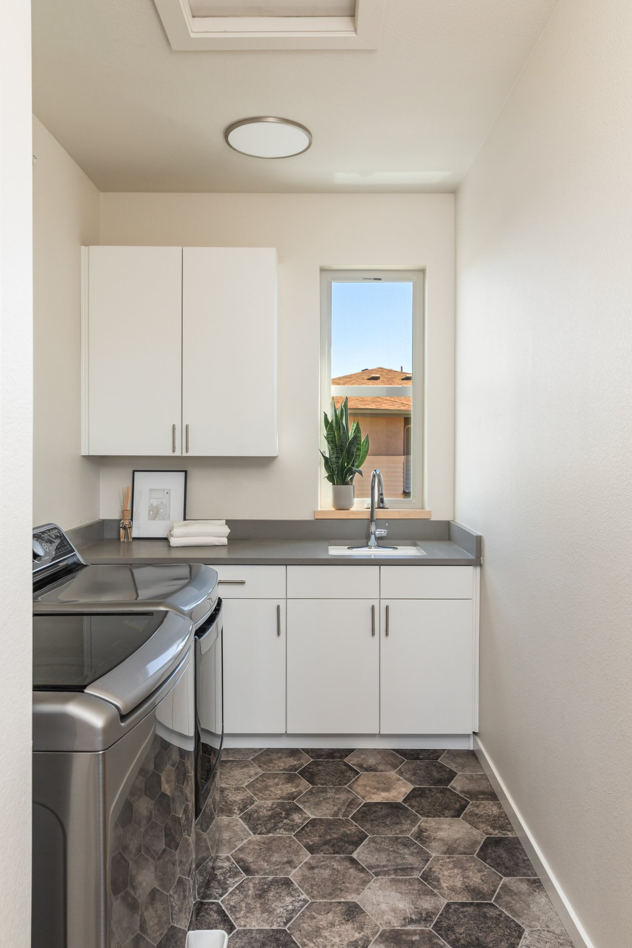 Laundry room with white cabinetry, a gray countertop, utility sink, and window