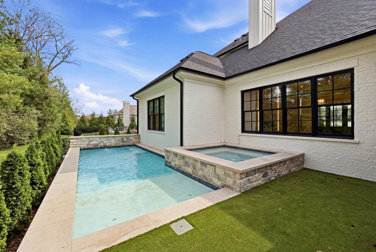 Backyard swimming pool with raised spa beside a white brick house.