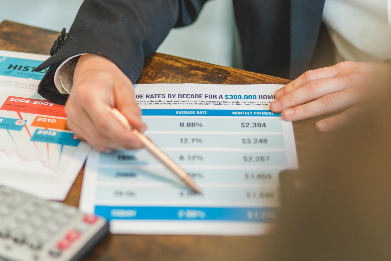 Hands point to a mortgage-rate chart beside a calculator.