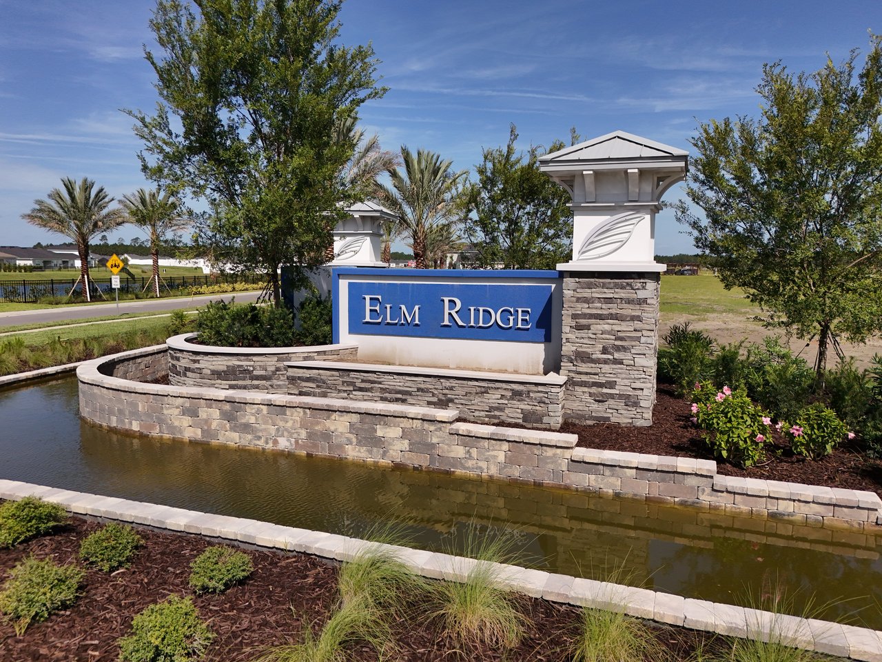 Elm Ridge community entrance sign beside a landscaped pond and stone wall.