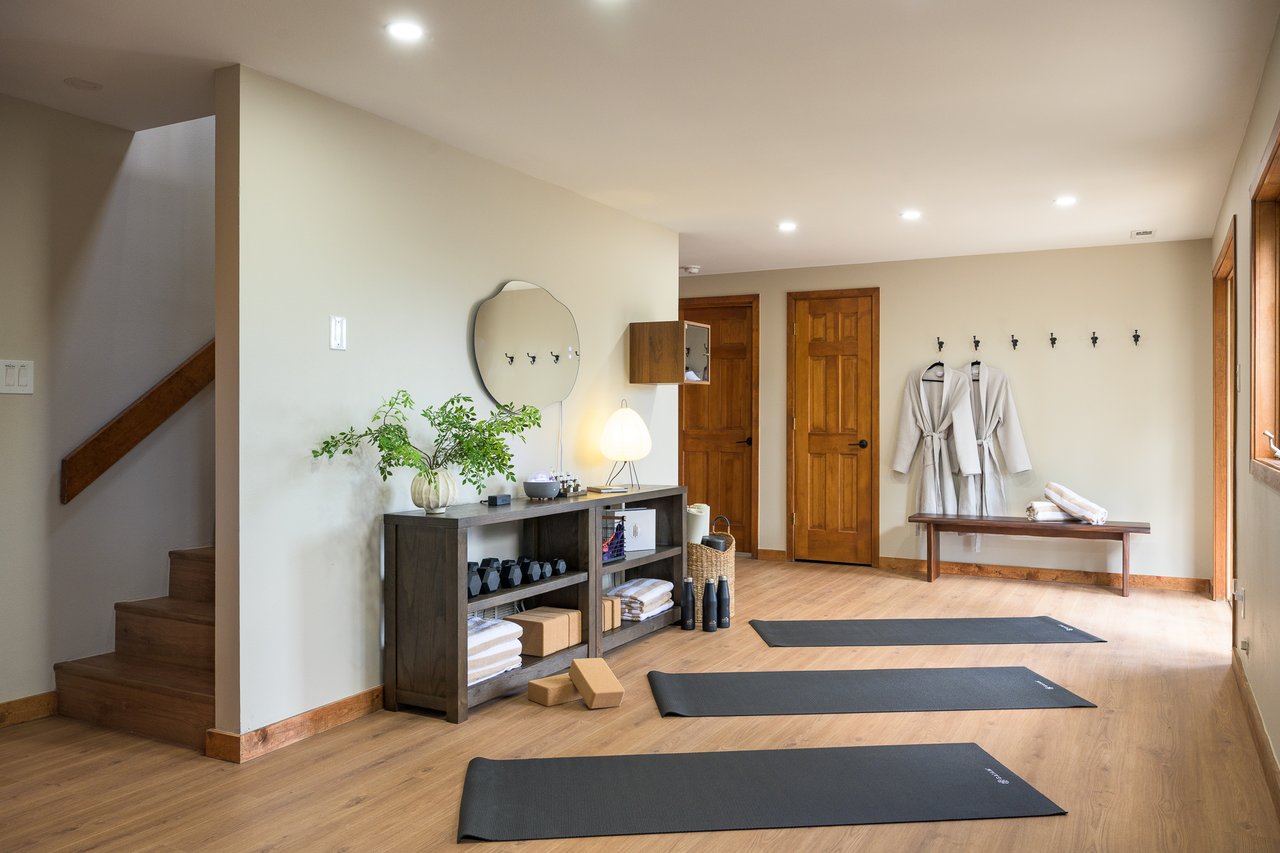 Home exercise room with three yoga mats, weights, hanging robes, and a staircase.
