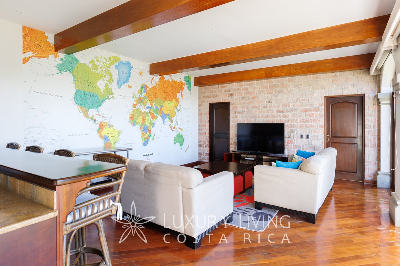Living room with a world map mural, exposed wooden beams, brick wall, and white seating.