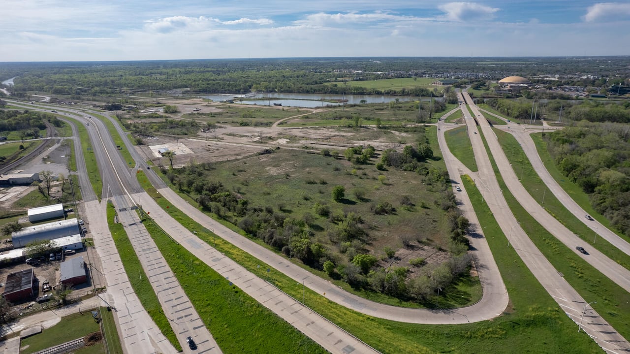 Aerial view of undeveloped land between divided highways, with a pond and commercial buildings nearby.