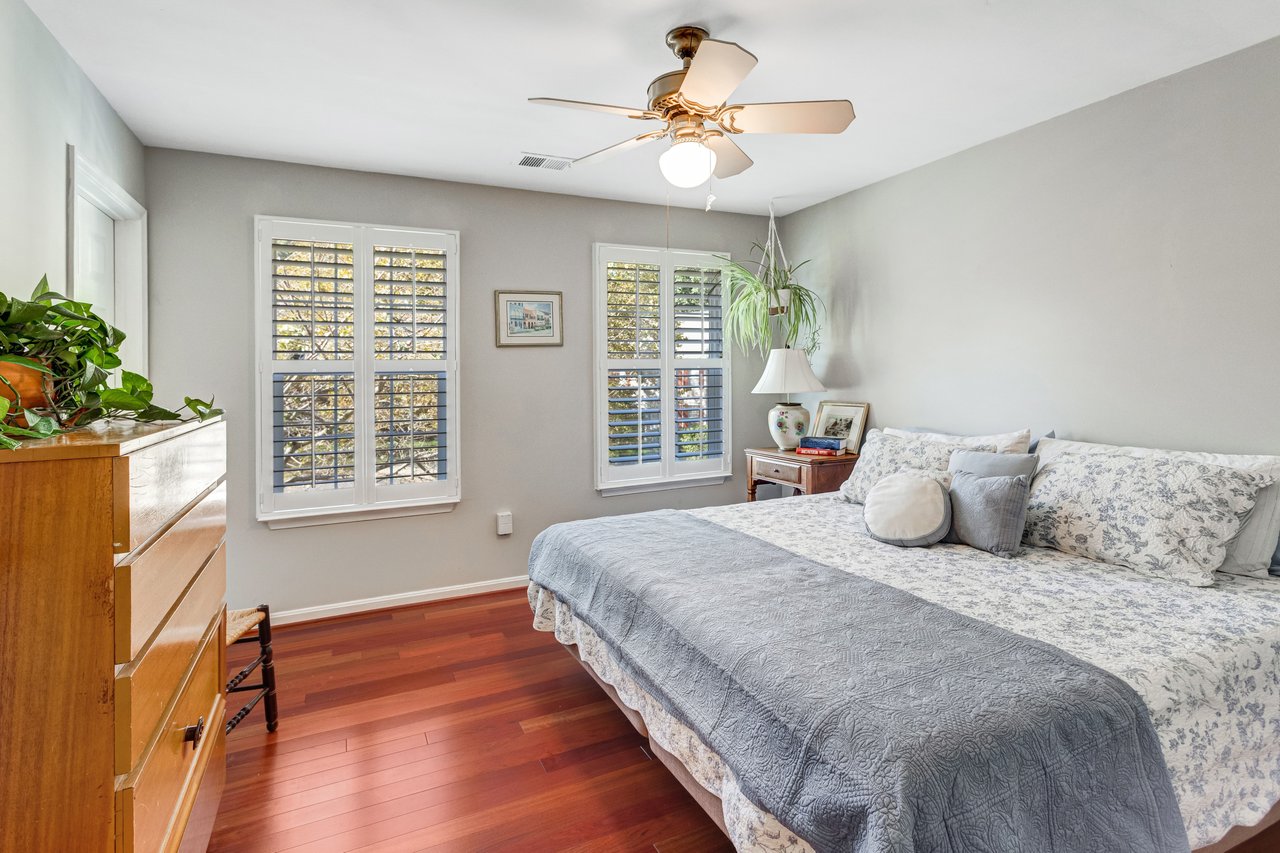 Bedroom with a floral bedspread, plantation shutters, and polished hardwood floors.