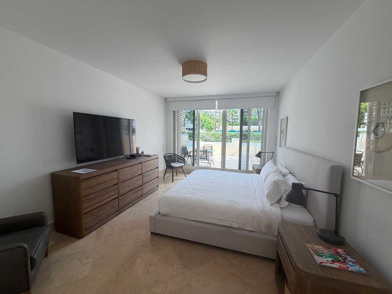 Bedroom with a king bed, wood dresser, and sliding doors overlooking a patio and pool.