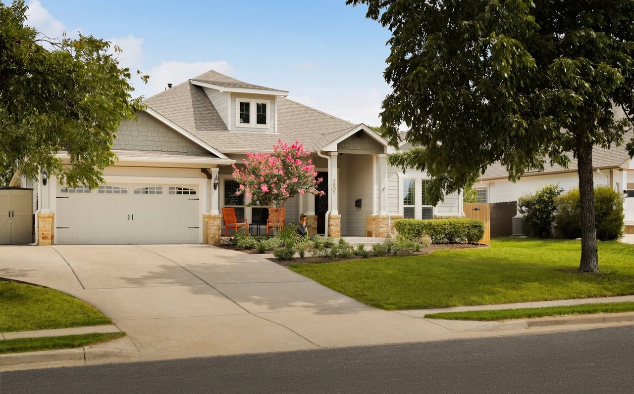 House exterior with a two-car garage, covered porch, and flowering pink tree.