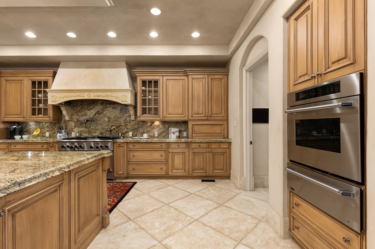 Traditional kitchen with honey-toned cabinetry, granite counters, and stacked stainless-steel ovens.