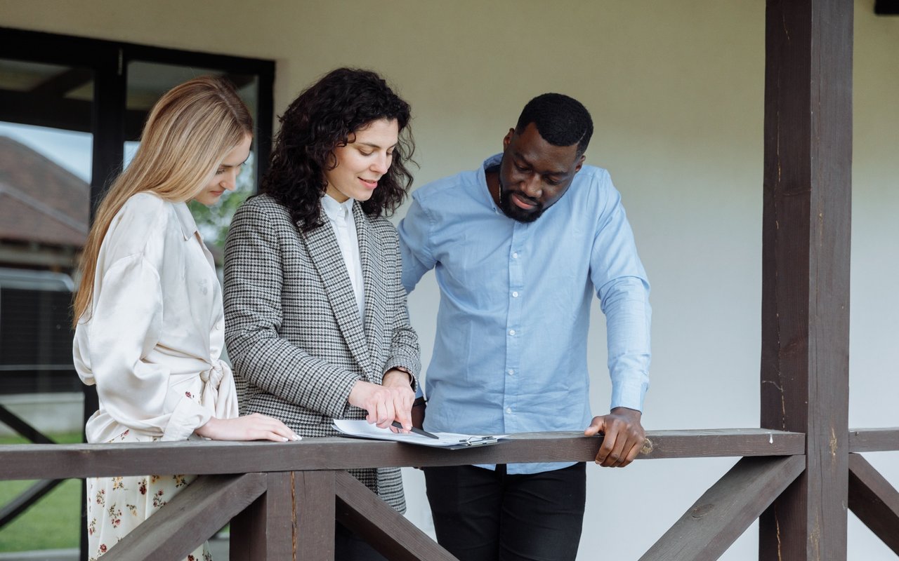 Three adults review paperwork together on a house porch.