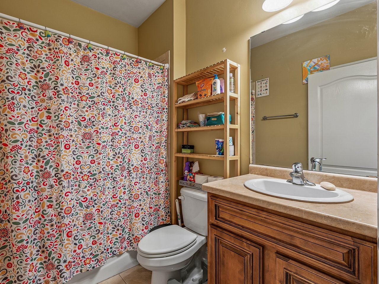 Bathroom with a colorful floral shower curtain, wood vanity, oval sink, and white toilet.